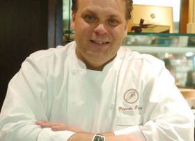 Chef in white uniform smiling behind a counter.