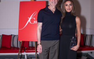 Man and woman posing together indoors with a red sign in the background.