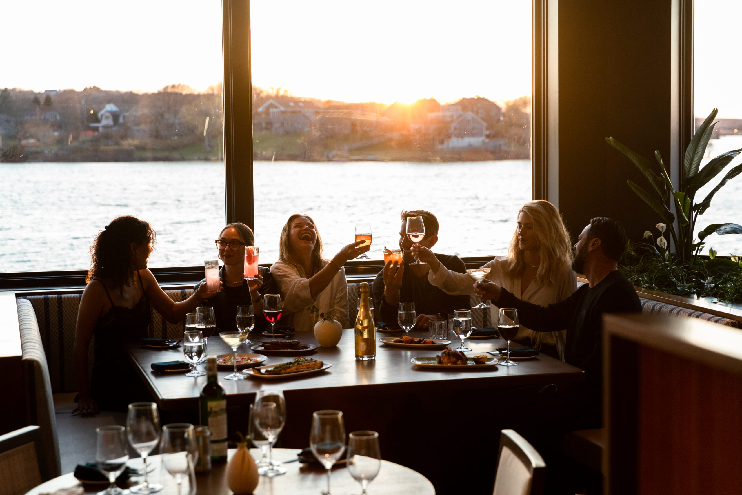 Group of friends toasting with drinks at sunset by the water.