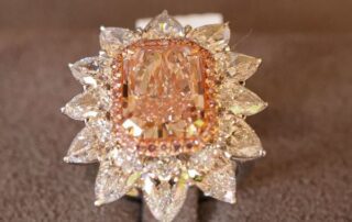 Close-up of a radiant diamond ring with a peach-colored center stone and surrounding white diamonds.