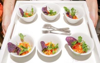 Six bowls of salad with purple chips and greens on a white tray with forks.