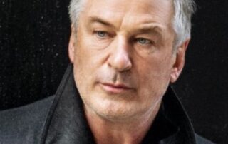 A man with gray hair wearing a black coat looks thoughtfully to the side.
