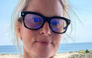 Woman wearing black glasses with ocean and beach background.