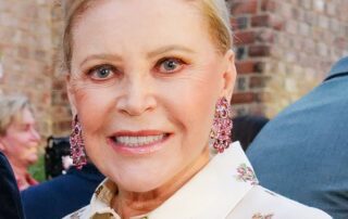 Elegant woman with blonde hair and floral blouse at an outdoor event.