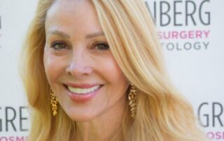 Smiling blonde woman with long hair and gold earrings.