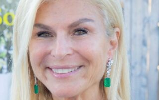 Smiling woman with long blonde hair and green earrings.