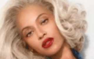 A woman with platinum blonde hair and bold red lipstick wearing a denim jacket.