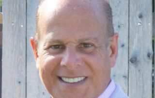 Smiling man in light blue blazer outdoors.