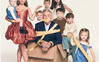 A man taped to a box surrounded by children and a smiling woman.