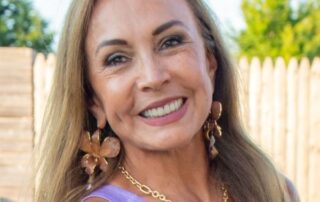 Smiling woman with long hair wearing a purple top and gold accessories.