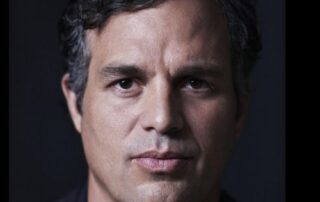 Close-up portrait of a man with dark hair against a dark background.