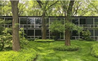 Modern glass building surrounded by lush green trees and manicured lawn.