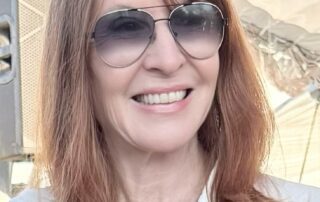 Smiling woman with red hair and sunglasses outdoors.