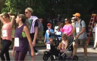 People walking outdoors, some pushing strollers, in casual attire.