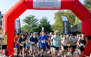 Runners starting a charity race under a red arch outdoors.