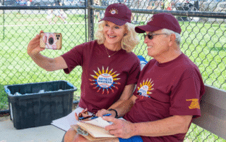 Two people in matching maroon shirts taking a selfie at an outdoor event.