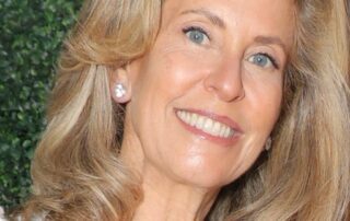 Smiling woman with blonde hair and pearl earrings.