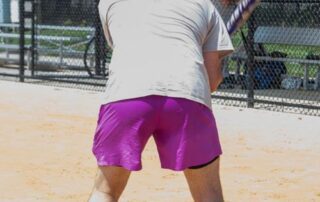 Man in purple shorts and gray shirt preparing to hit a baseball.