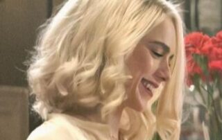 Smiling woman with blonde wavy hair in a soft-lit setting.