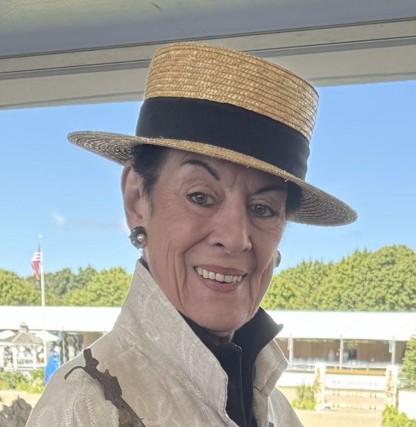 Elegant woman wearing a straw hat with a black band, smiling outdoors.