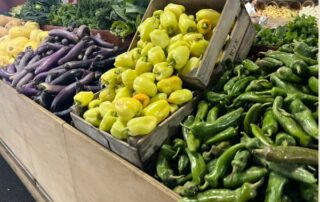 Fresh green, yellow peppers, and eggplants displayed at a market stall.