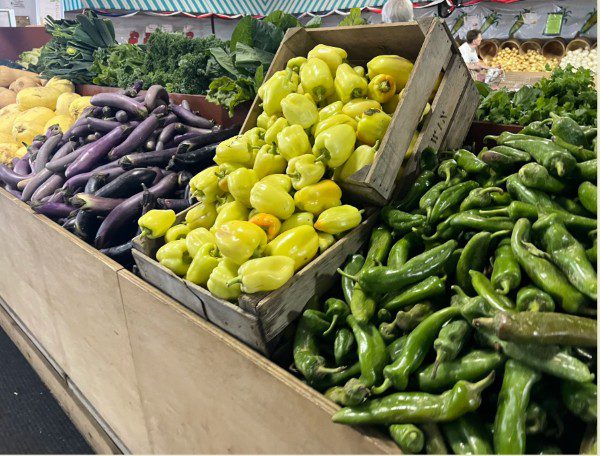 Fresh green, yellow peppers, and eggplants displayed at a market stall.