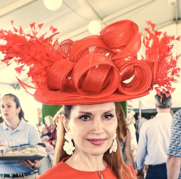 Woman wearing an elaborate red hat and matching dress at an event.