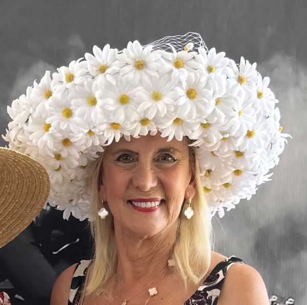 Woman wearing a large hat made of white daisies, smiling.