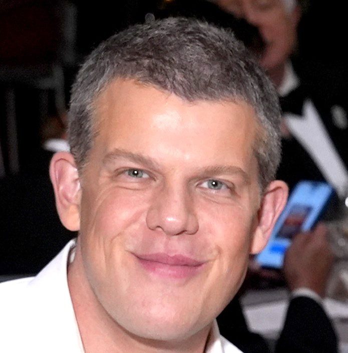 A smiling man with short hair and a white shirt at an event.