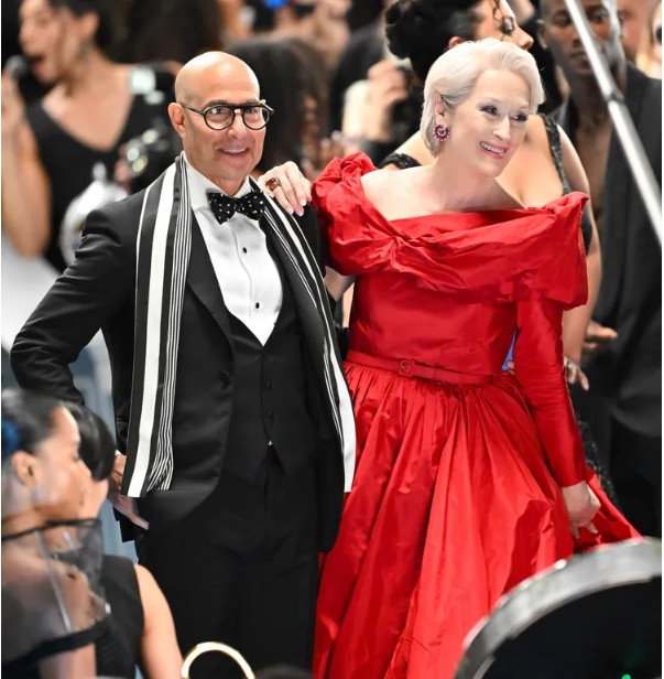 A man in a tuxedo and a woman in a red dress pose at a formal event.